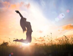 silhouette d'une femme qui saute en l'air dans l'herbe, devant un coucher de soleil