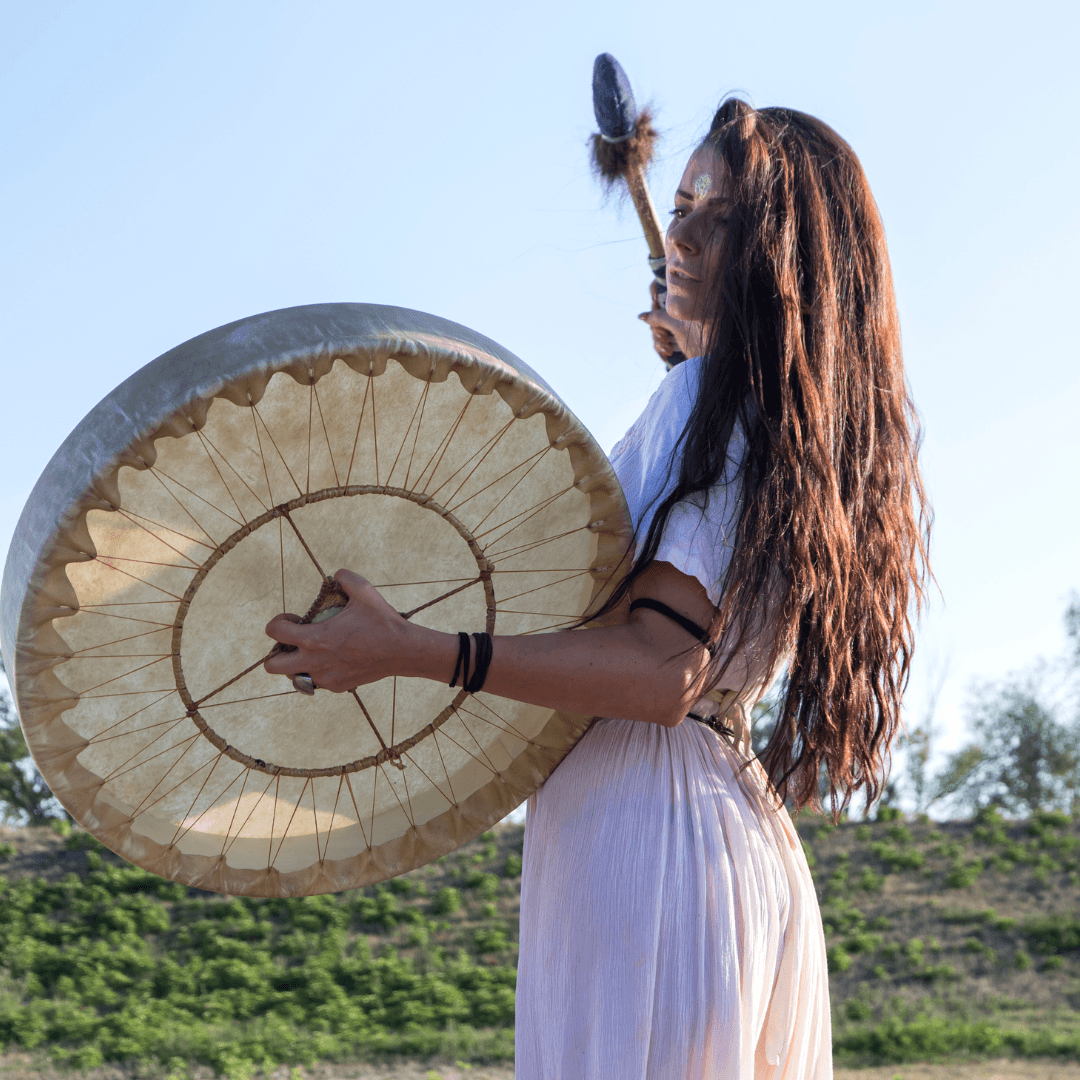 une femme joue du tambour chamanique dans la nature